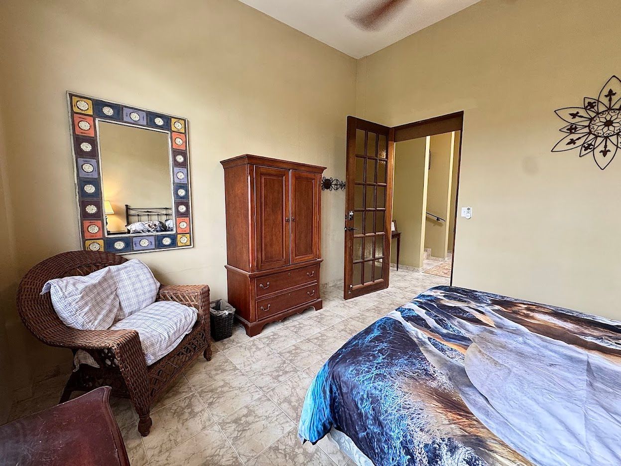 Bedroom with wooden armoire, wicker chair, and open doorway.