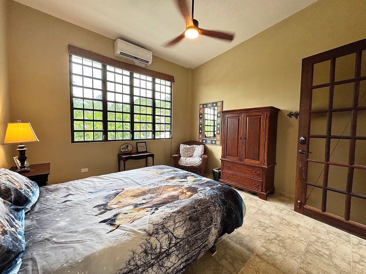 Bedroom with bed, closet, window, and door. Earth-toned walls, ceiling fan, and tile floor.