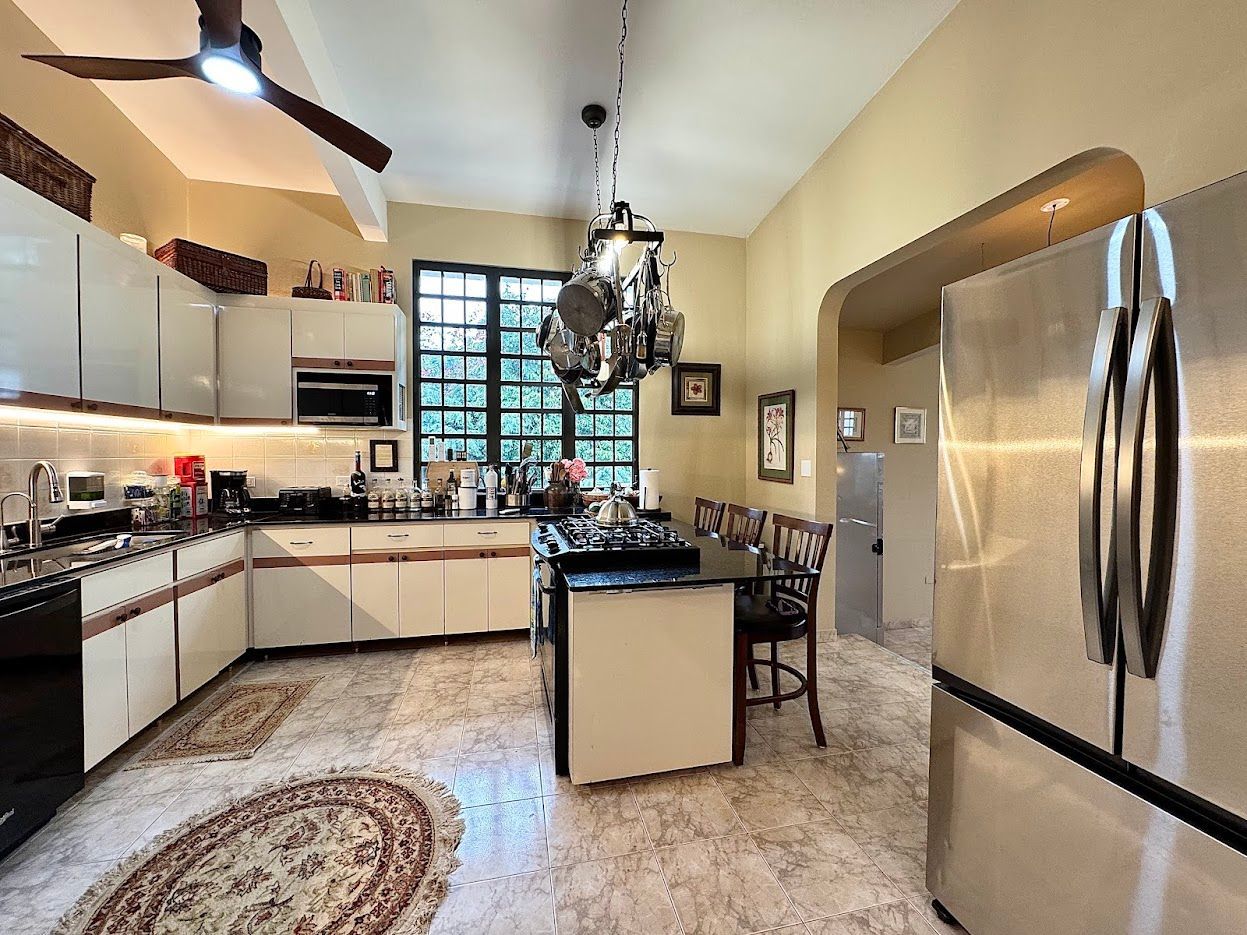 Kitchen with white cabinets, dark island, stainless steel refrigerator, and round rug.