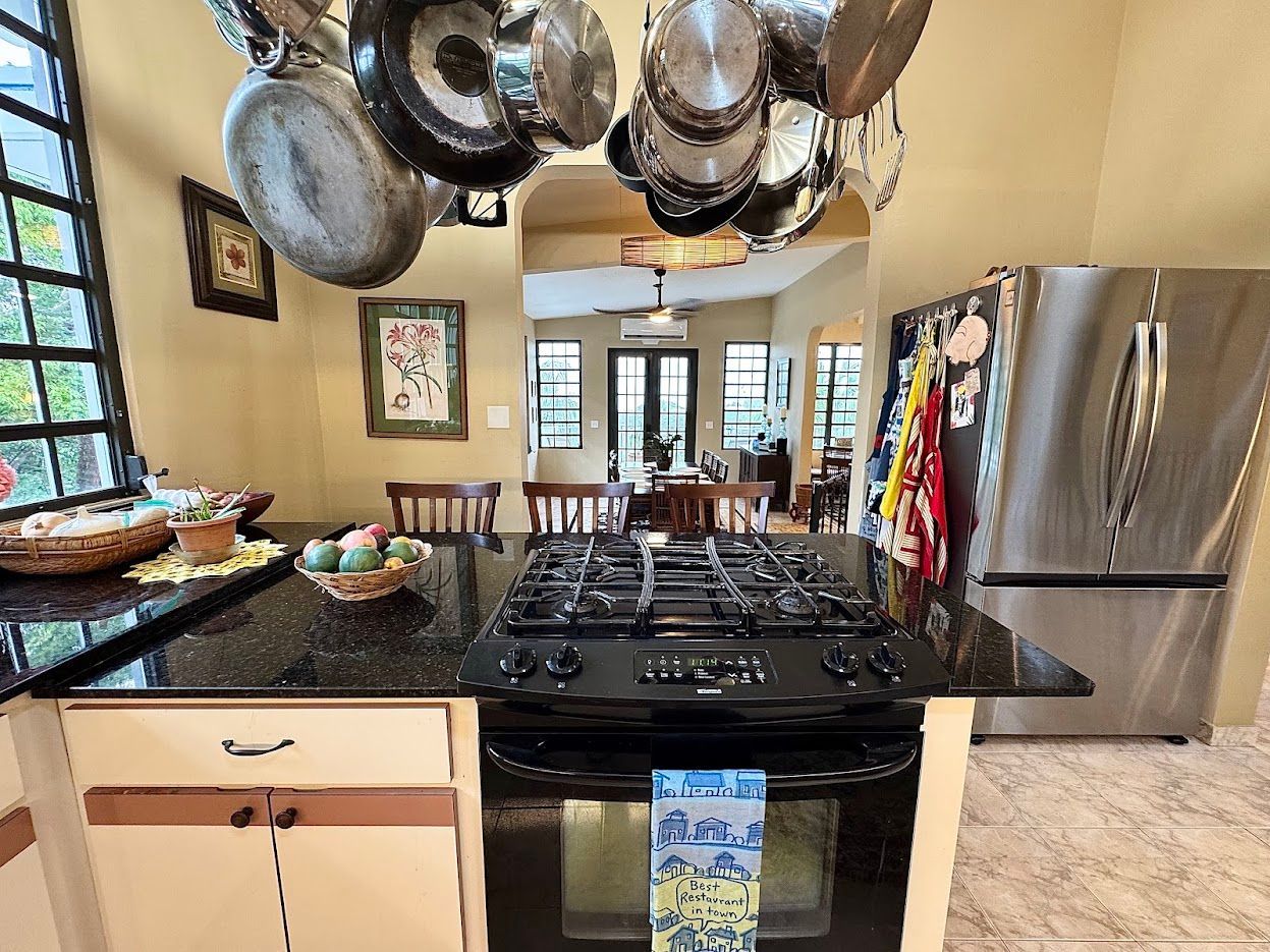 Kitchen with stove, pots hanging overhead, black countertop, refrigerator, and doorway to a dining room.
