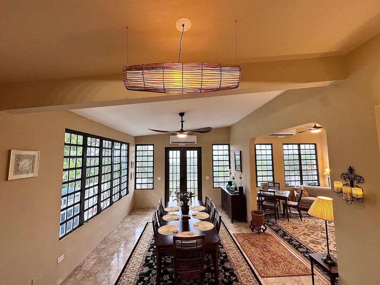 Dining room with long table, windows, archway to seating area, and decorative light fixtures.