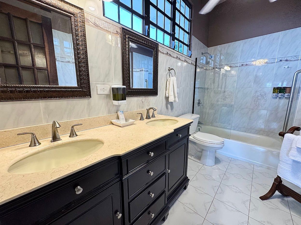 Bathroom with black vanity, two sinks, mirrors, tub, and window.
