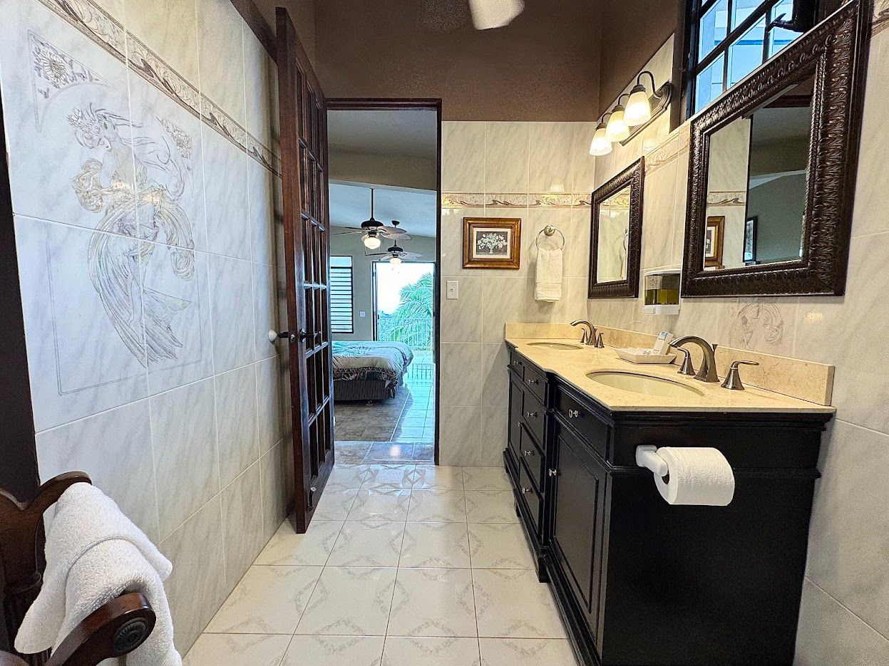 Bathroom with a dark vanity, two sinks, and a doorway leading to a bedroom.
