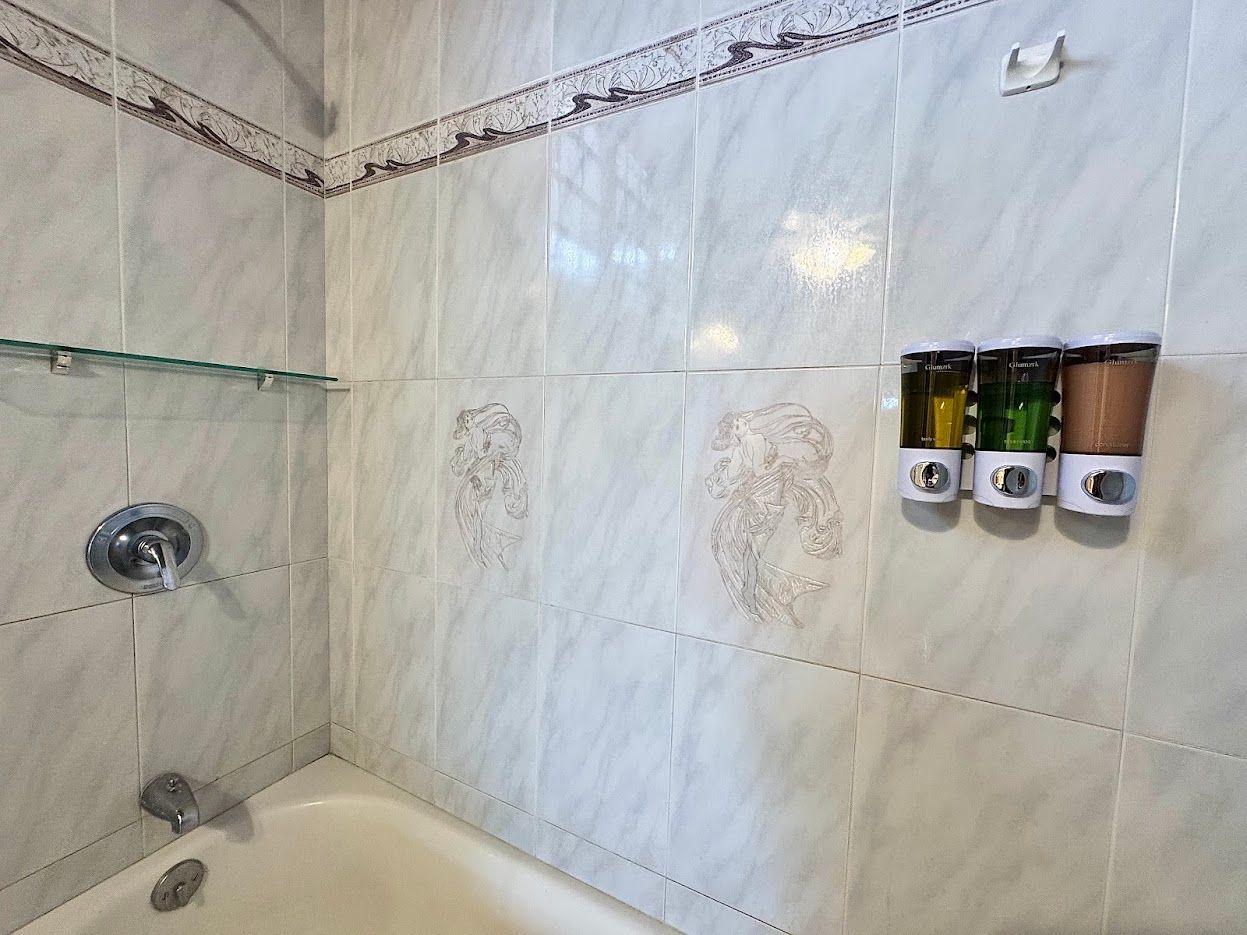 Bathroom with white tiled walls, bathtub, shower fixtures, and soap dispensers.