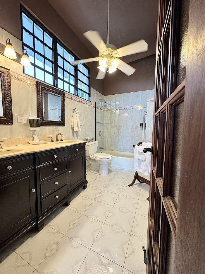 Bathroom with dark wood vanity, white tile floor, shower, and window with a fan.