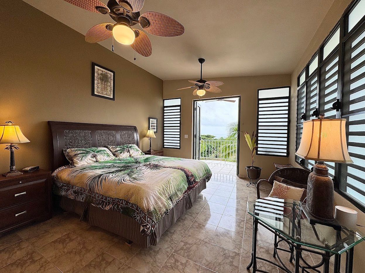Bedroom with two beds, ceiling fans, open door to balcony, and windows with horizontal blinds.
