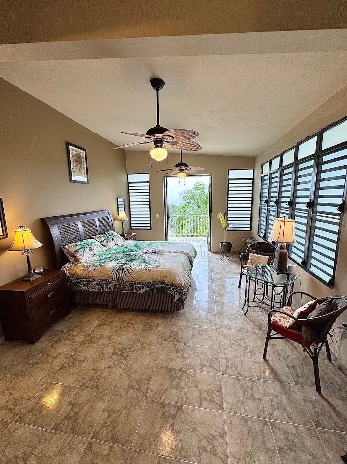 Bedroom with a bed, two lamps, chairs, and large windows with a view.