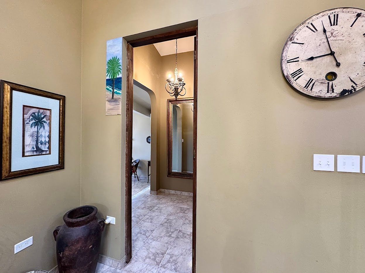 Hallway with artwork, an ornate clock, and an open doorway leading to a mirror and chandelier.