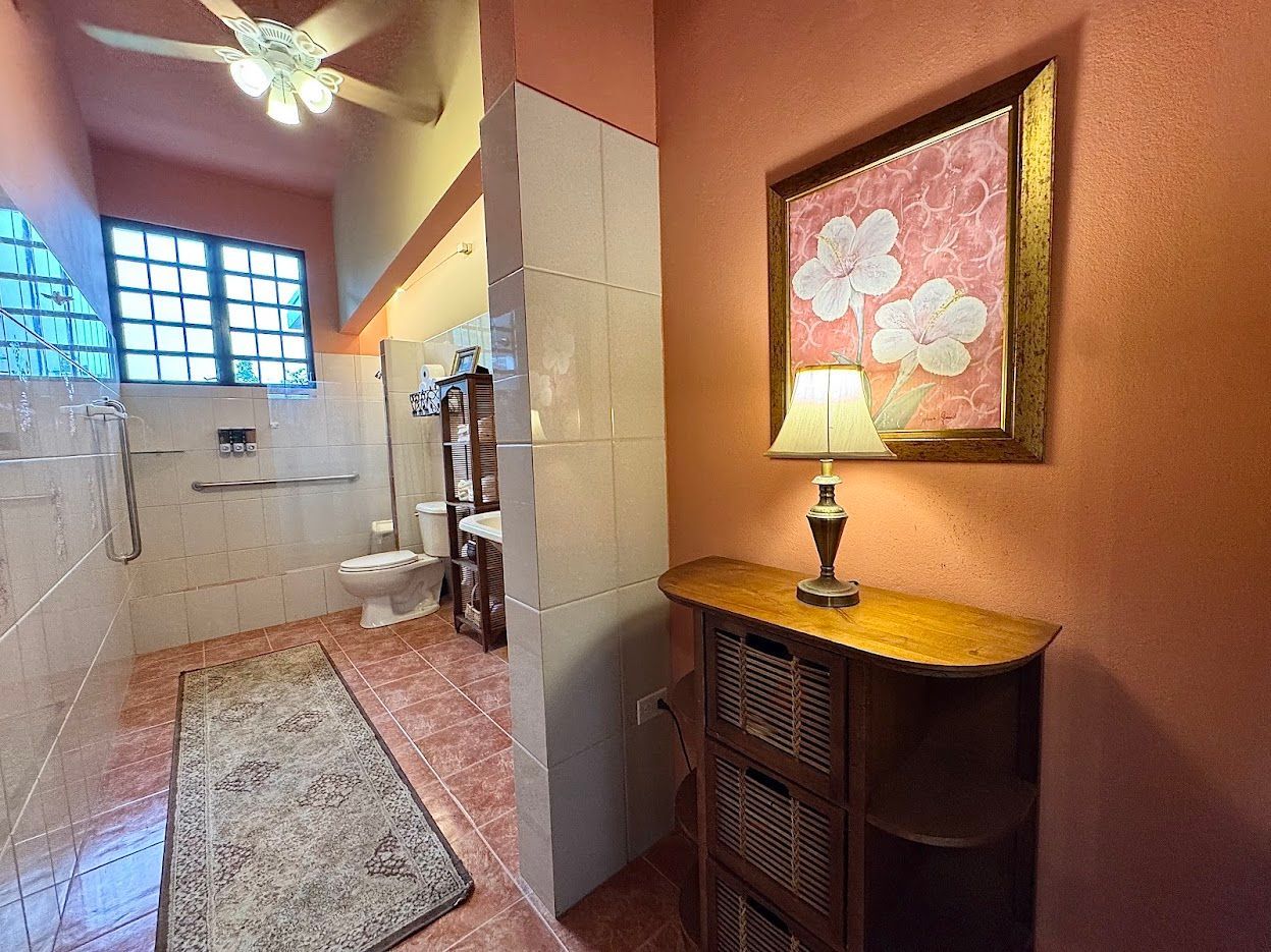 Bathroom with an open doorway, showing a toilet and a decorative cabinet with a painting and a lamp.