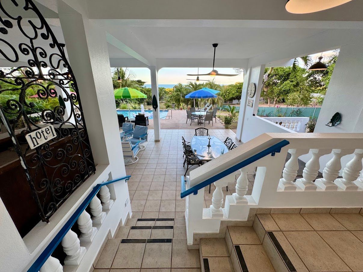 Exterior view of a hotel, featuring a pool, dining area, and ocean view.