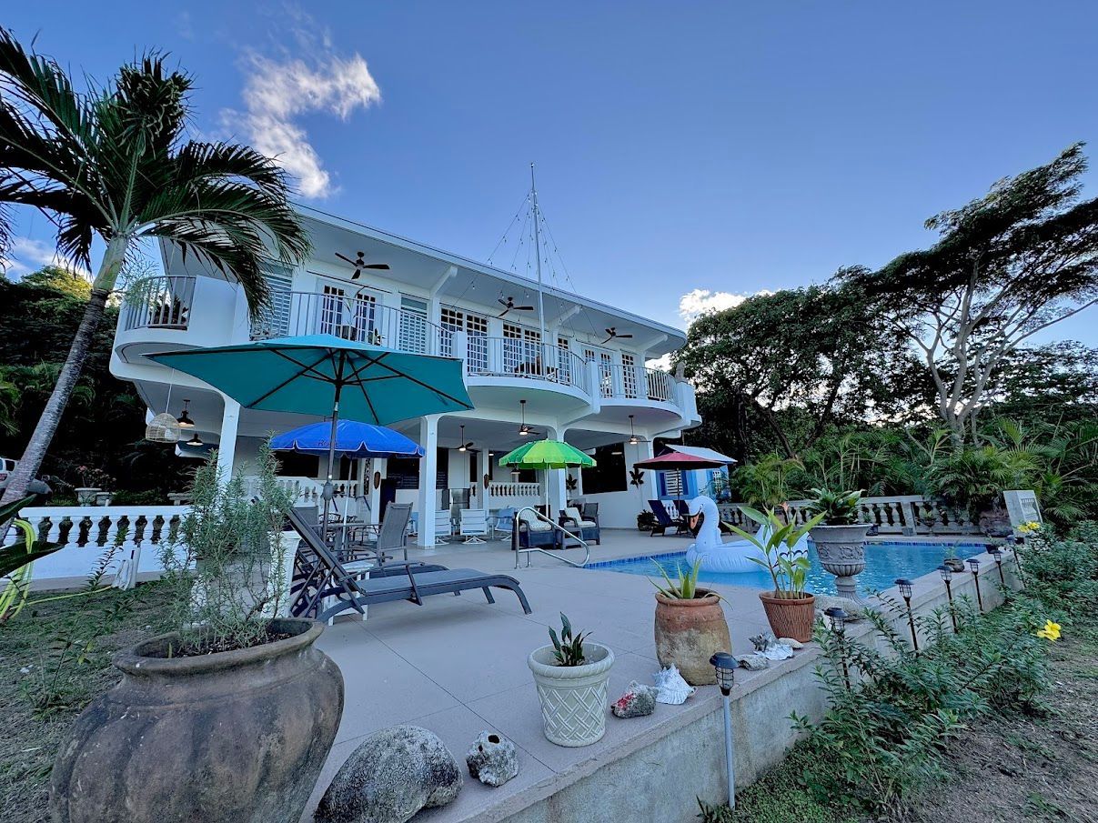 White house with a pool, patio furniture, and blue sky.