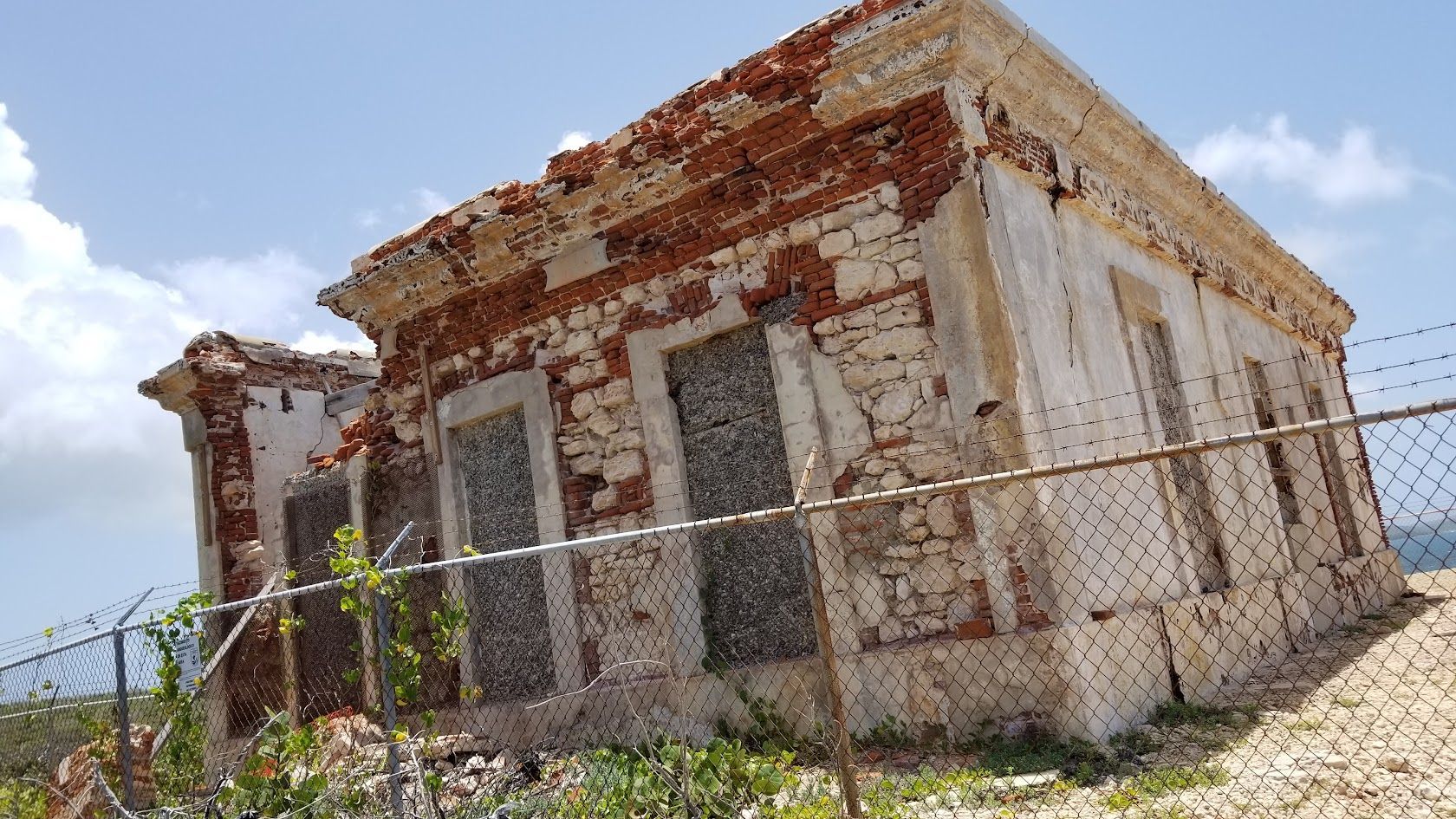 People dining at waterside restaurants at dusk, wooden dock, palm trees, colorful buildings.