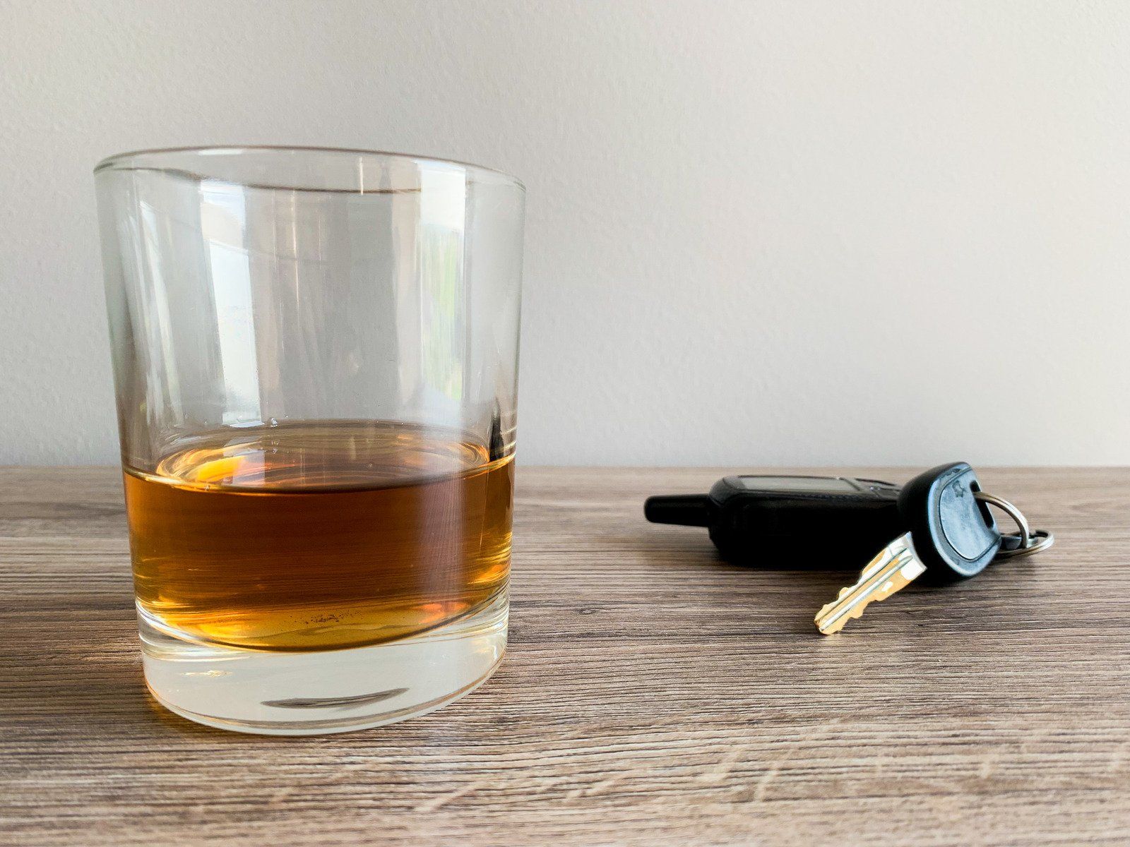 Glass of amber liquor next to car keys on a wooden surface.