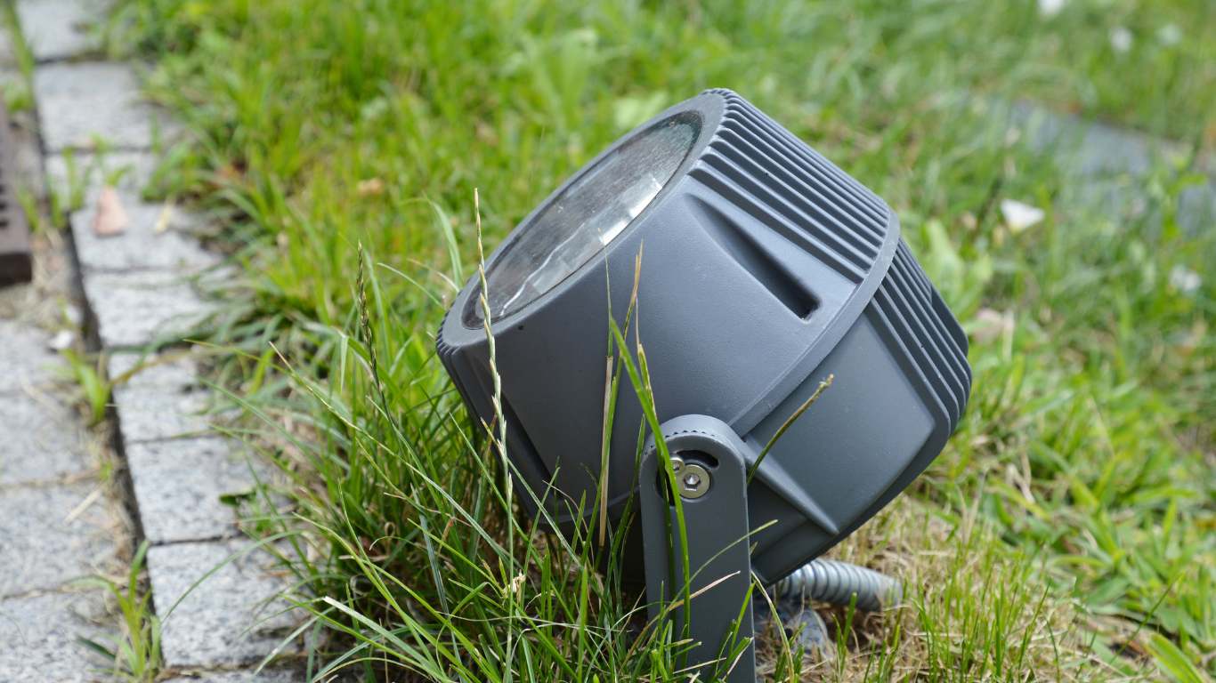 A spotlight is sitting in the grass next to a sidewalk.