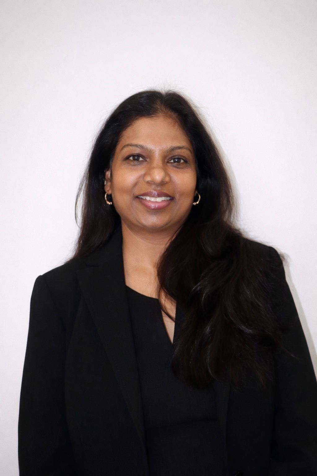 Woman with red hair smiling, wearing a white blazer and black top.