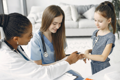 Doctor examines a child's wrist with a nurse present. They are in an office setting.