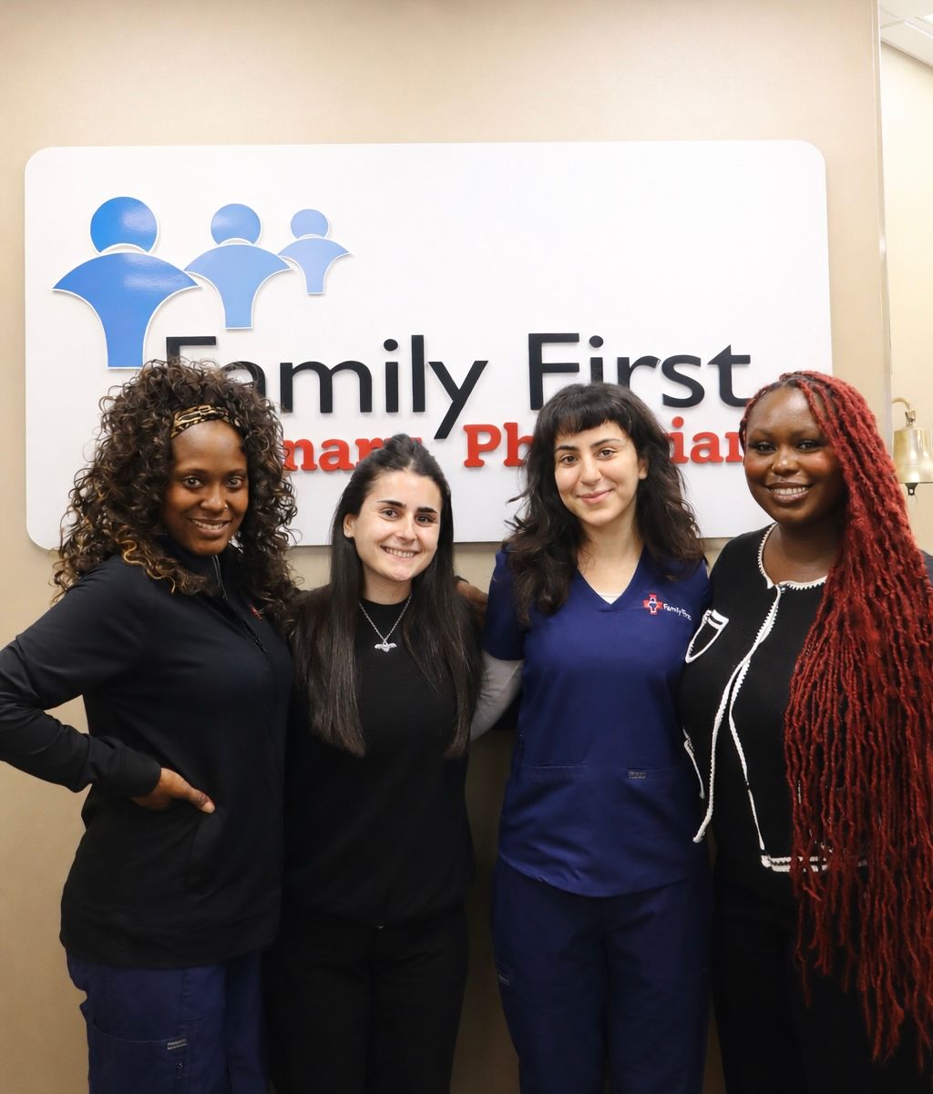 Four people stand in front of a Family First Primary Physicians sign. Two wear scrubs, and one wears a jacket.
