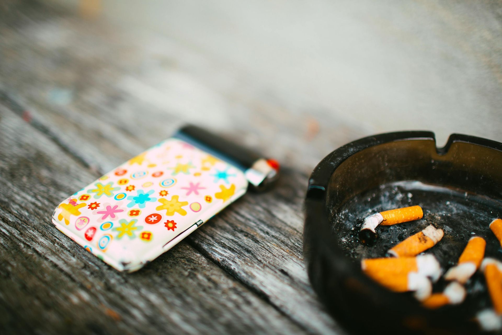 Floral-patterned cigarette case beside an ashtray with cigarette butts on a wooden table