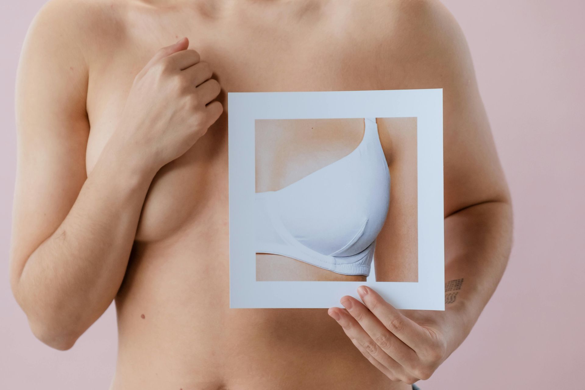 Person holding a cutout frame over their torso, revealing a breast implant illustration inside