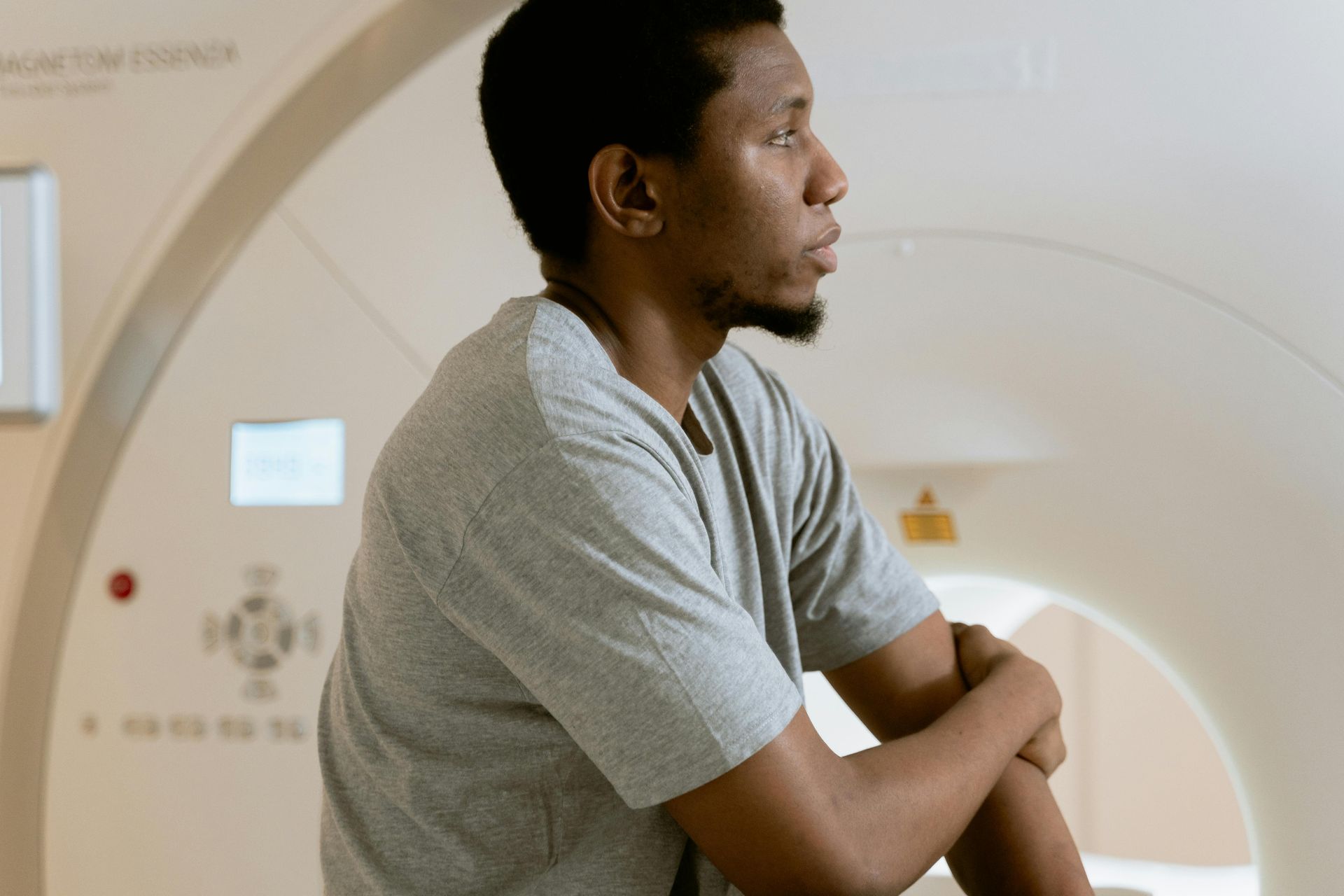 Person in a gray shirt leaning on a large white medical imaging scanner in a clinical setting