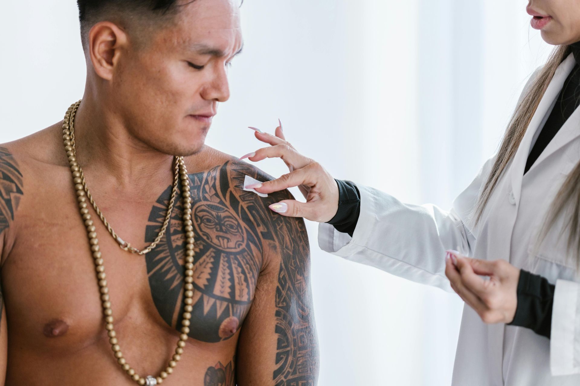 Health professional examining a man’s chest tattoo with a pen in a bright clinic setting