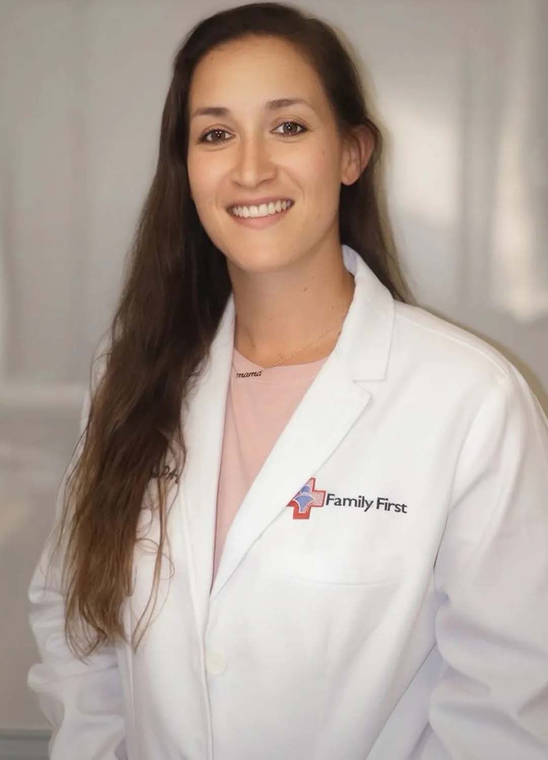 Woman in white lab coat smiles; Family First logo on coat.