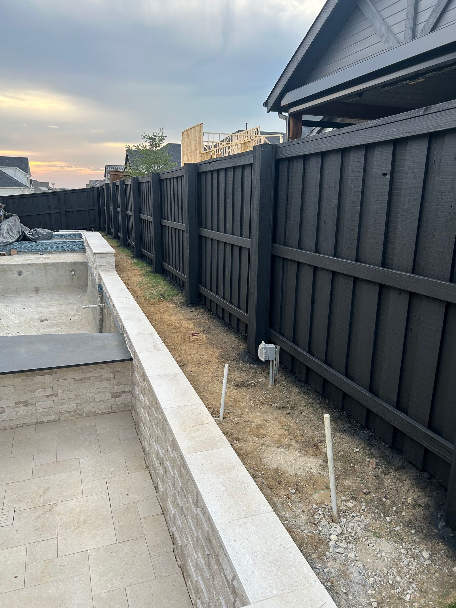 Backyard with concrete steps, gravel border, and black fence beside a house at sunset