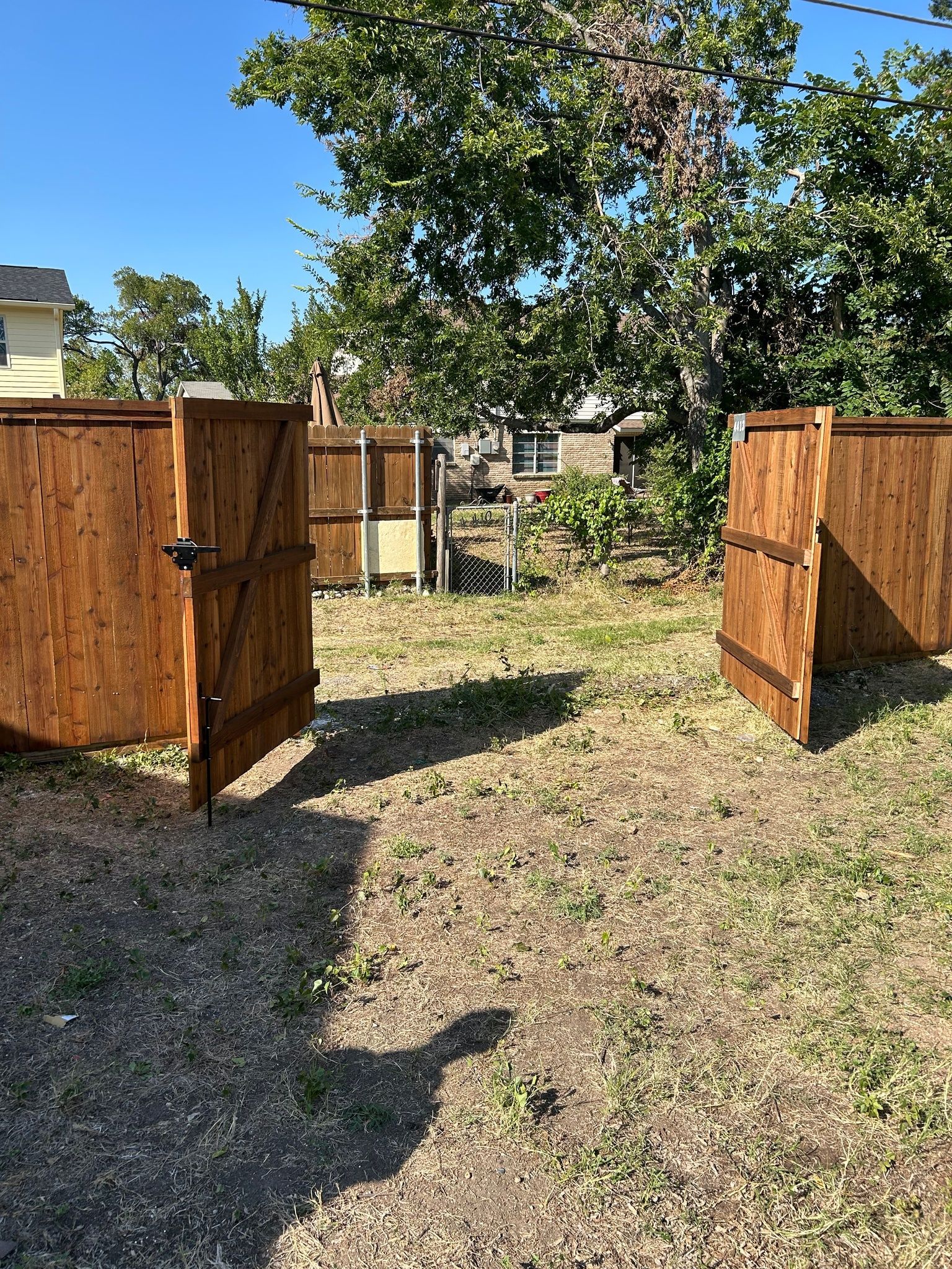 Open wooden gates in a sunny backyard with a tree and gravel path