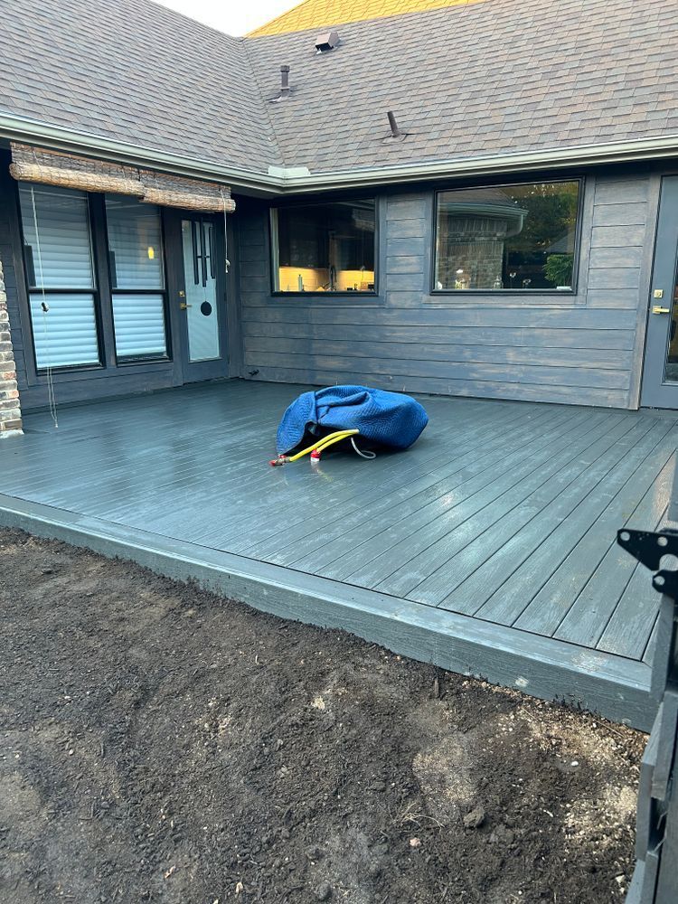 Backyard deck with a covered object, gray house exterior, and bare dirt in the foreground