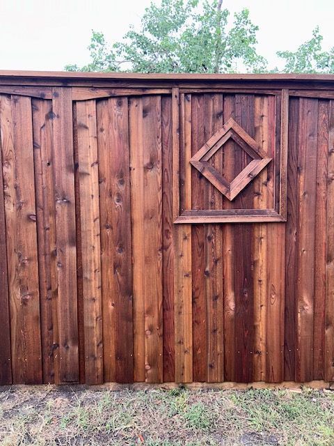 Wooden fence with a decorative diamond panel and trees visible above it
