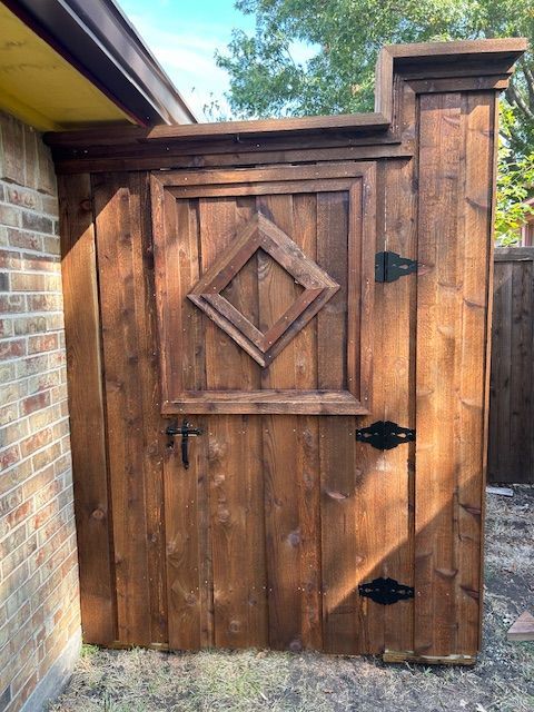 Wooden gate with diamond panel and black hardware beside a brick wall outdoors