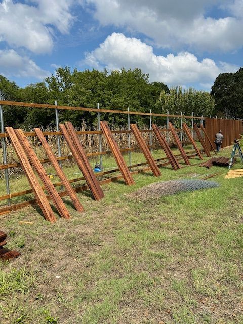 Wooden fence panels drying on grass beside a fence under a partly cloudy sky