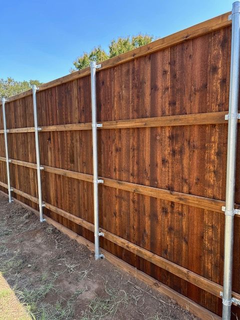 Wooden privacy fence with metal posts along a dirt yard under a blue sky