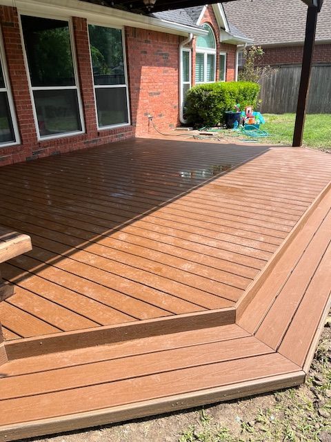 Wooden backyard deck with raised edge beside a brick house and windows