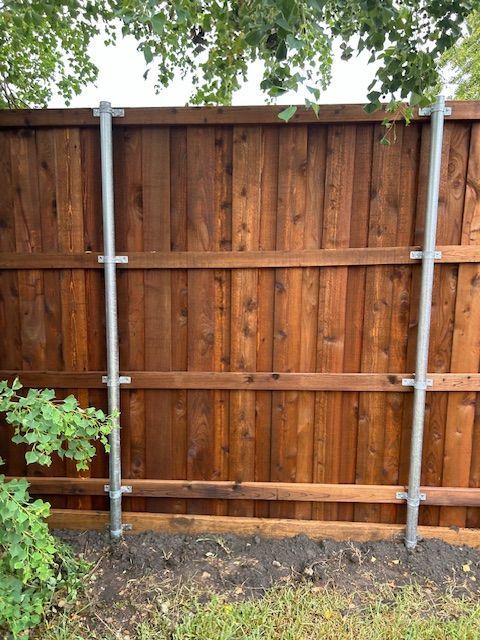 Wooden privacy fence with gray metal posts in a backyard, with trees and shrubs around it