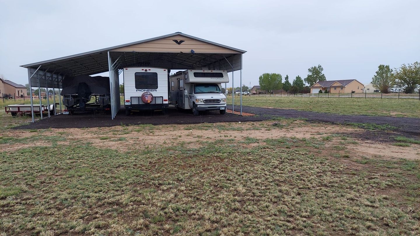 A rv is parked under a shed in a field.