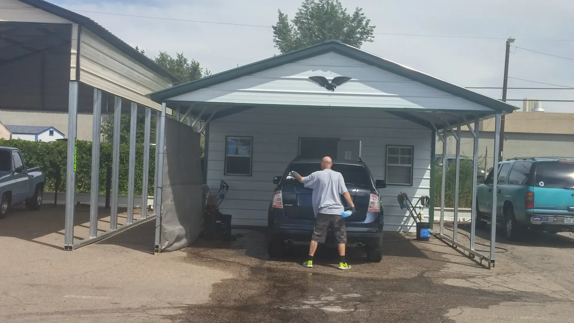 A row of cars parked under a steel carport.