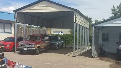 A carport with a flat roof and a garage with a wooden door, with cars parked in and under each.