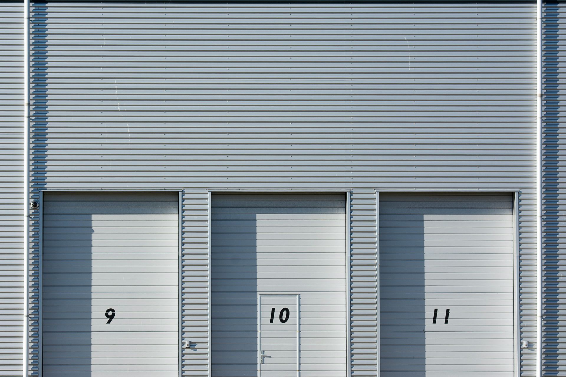 Three gray industrial doors labeled 9, 10, and 11 on a corrugated metal building.