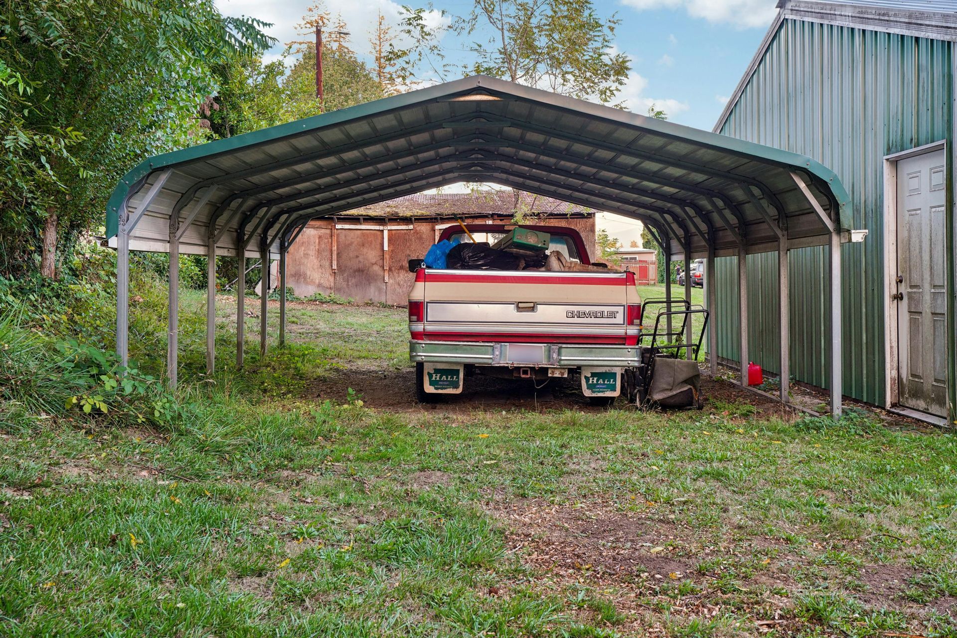 A modern carport attached to a suburban house, with a black sedan and a silver SUV parked underneath