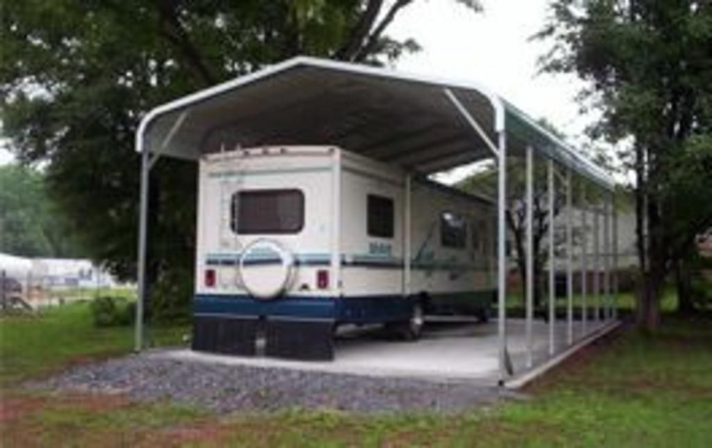 A white and blue rv is parked under a carport.