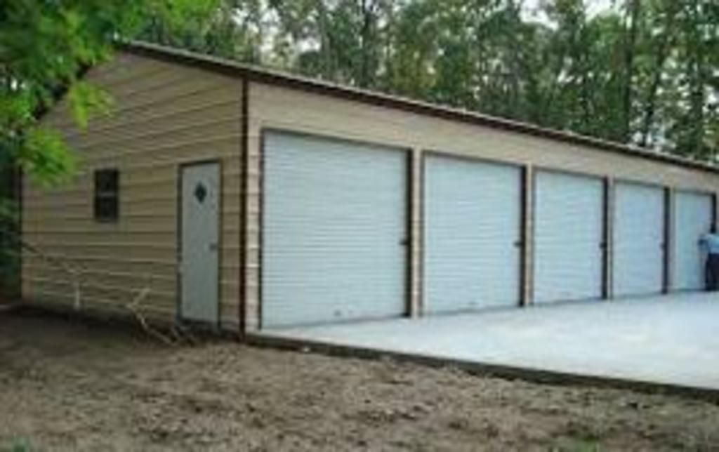 A large metal garage with white garage doors and a concrete driveway.