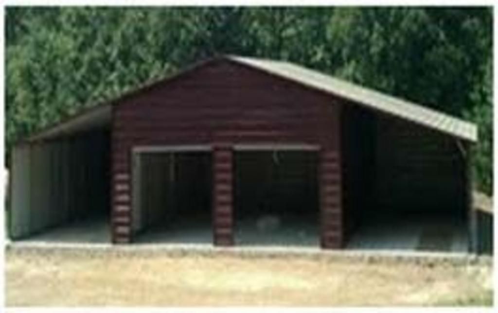 A large brown garage with three doors is sitting in the middle of a field.