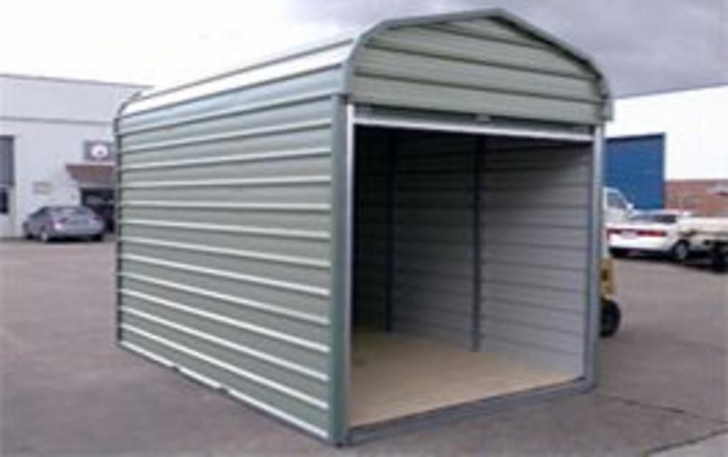 A small metal shed is sitting in a parking lot next to a building.