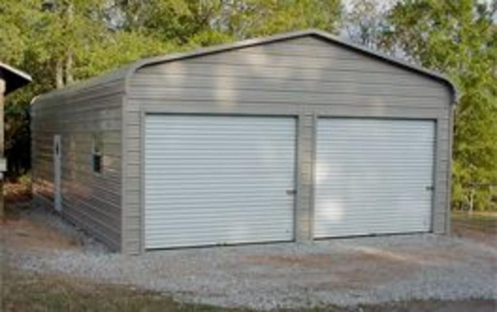 A metal garage with two white garage doors is sitting on top of a gravel lot.