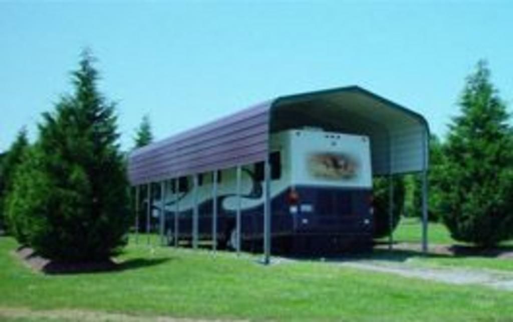 A blue and white bus is parked under a carport.