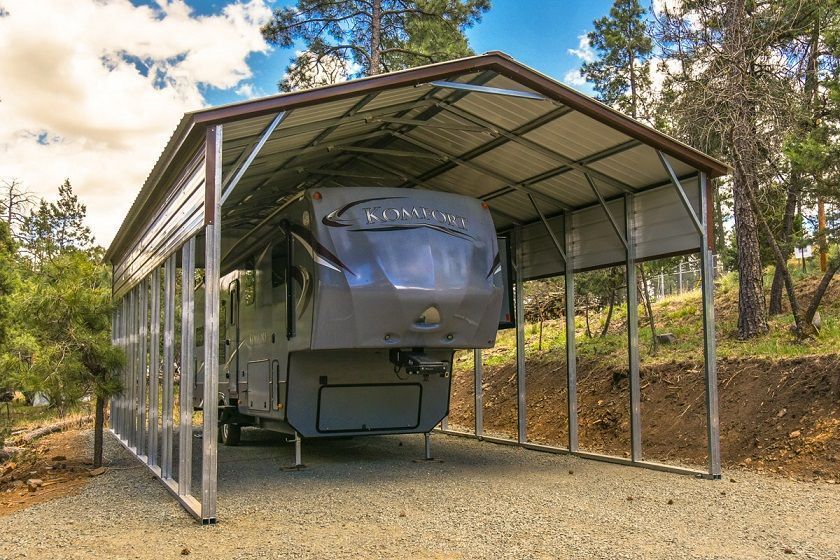 A rv is parked under a metal carport.