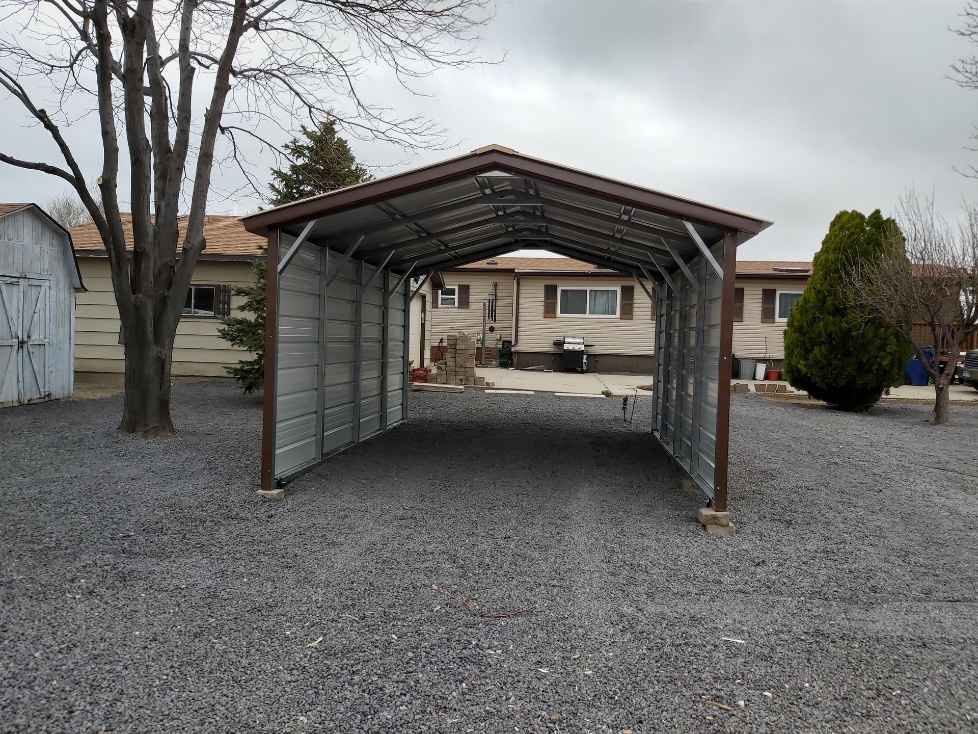 A carport is sitting in the gravel in front of a house