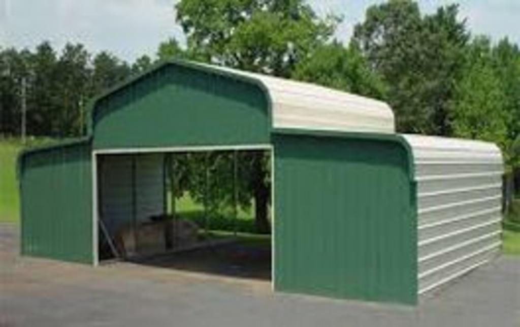 A green barn with a white roof is sitting on top of a dirt road.