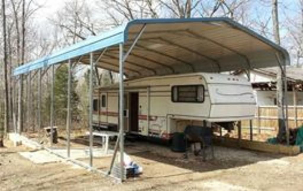 A white rv is parked under a blue canopy.